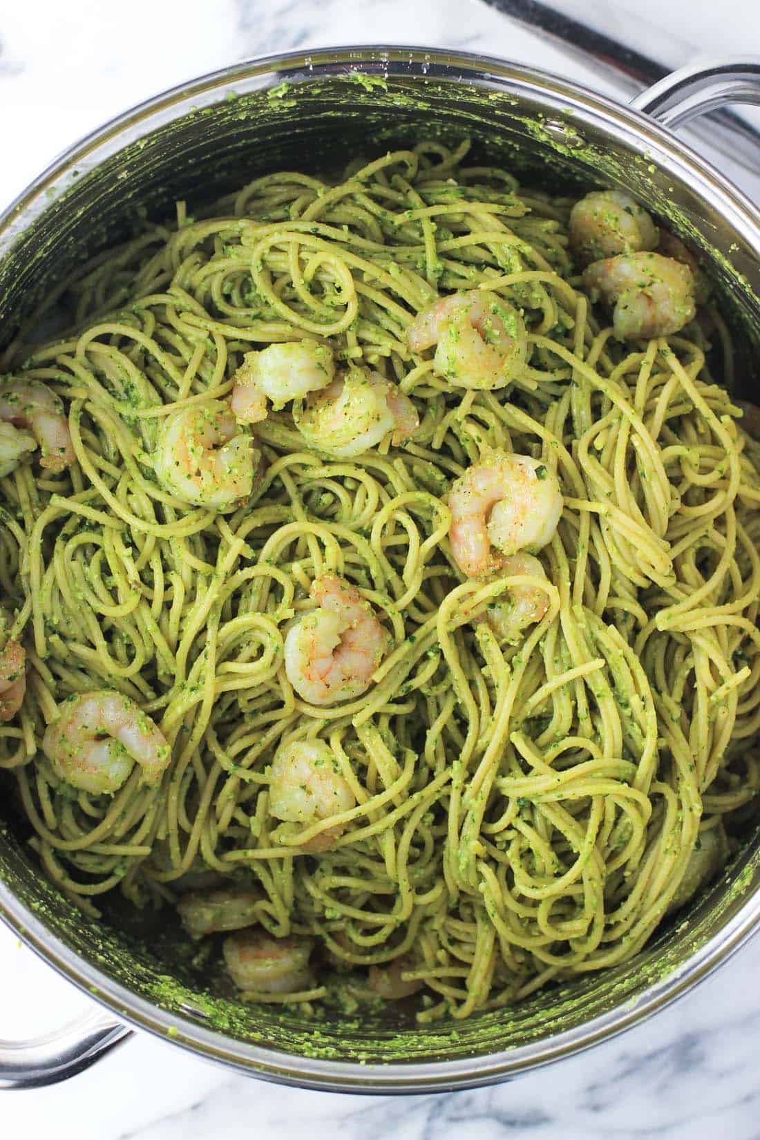 An overhead shot of a large metal pot of pesto pasta topped with srhimp