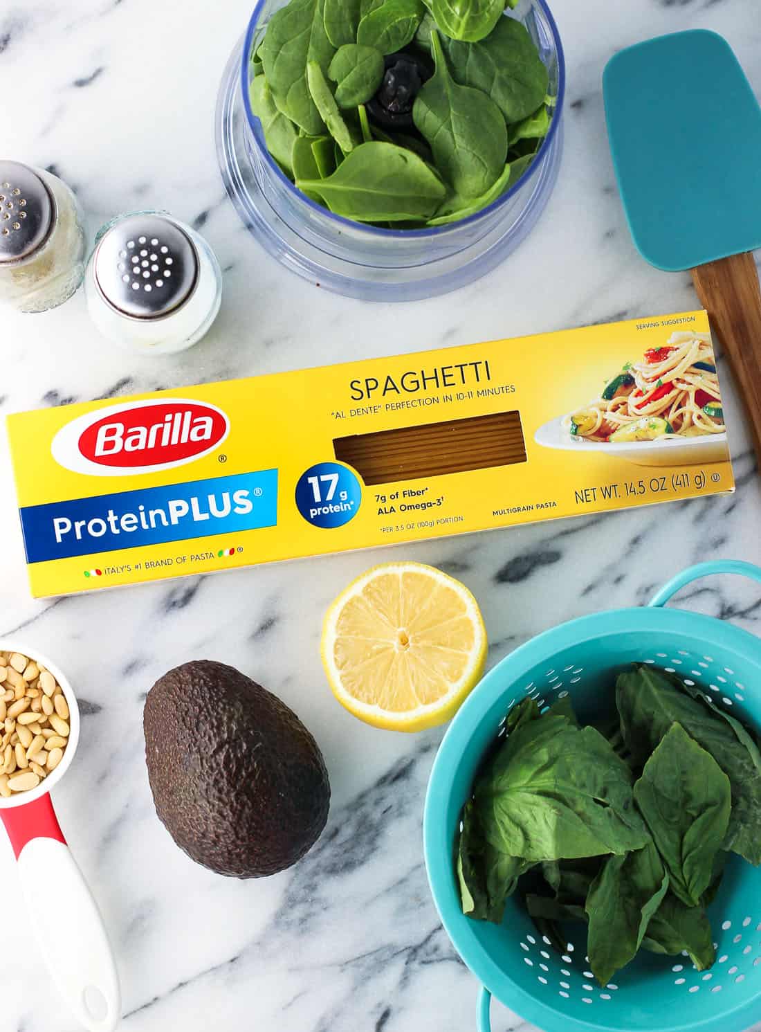 An overhead shot of the recipe ingredients on a marble board surrounding a box of Barilla ProteinPLUS spaghetti