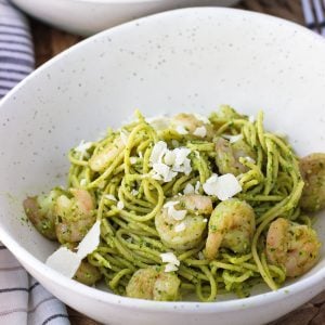 A bowl of spaghetti coated in pesto sauce topped with shrimp and shaved Parmesan cheese