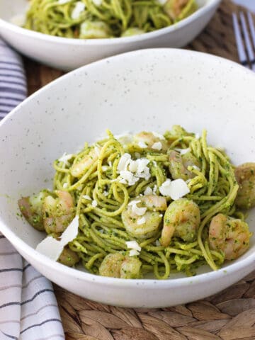 A bowl of spaghetti coated in pesto sauce topped with shrimp and shaved Parmesan cheese