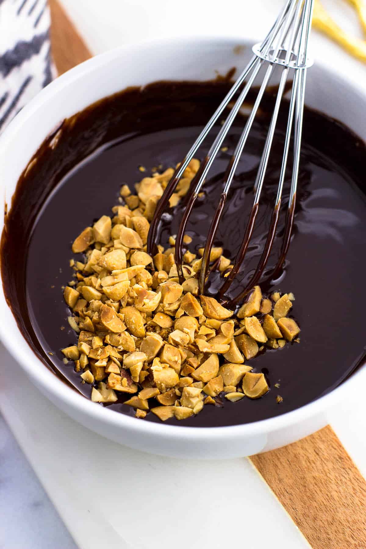 The melted chocolate/butter/cream/peanut butter mixture in a bowl with chopped peanuts on top and a whisk