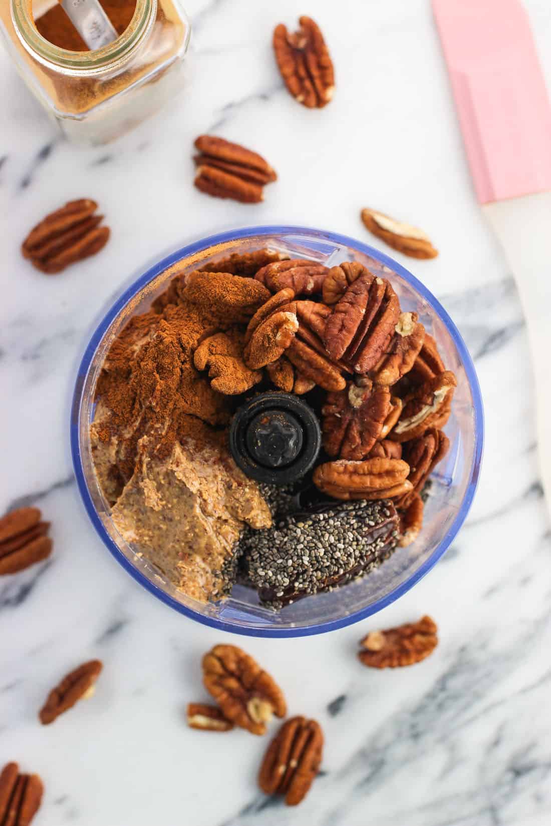 Pecans, dates, and other recipe ingredients in the bowl of a food processor.