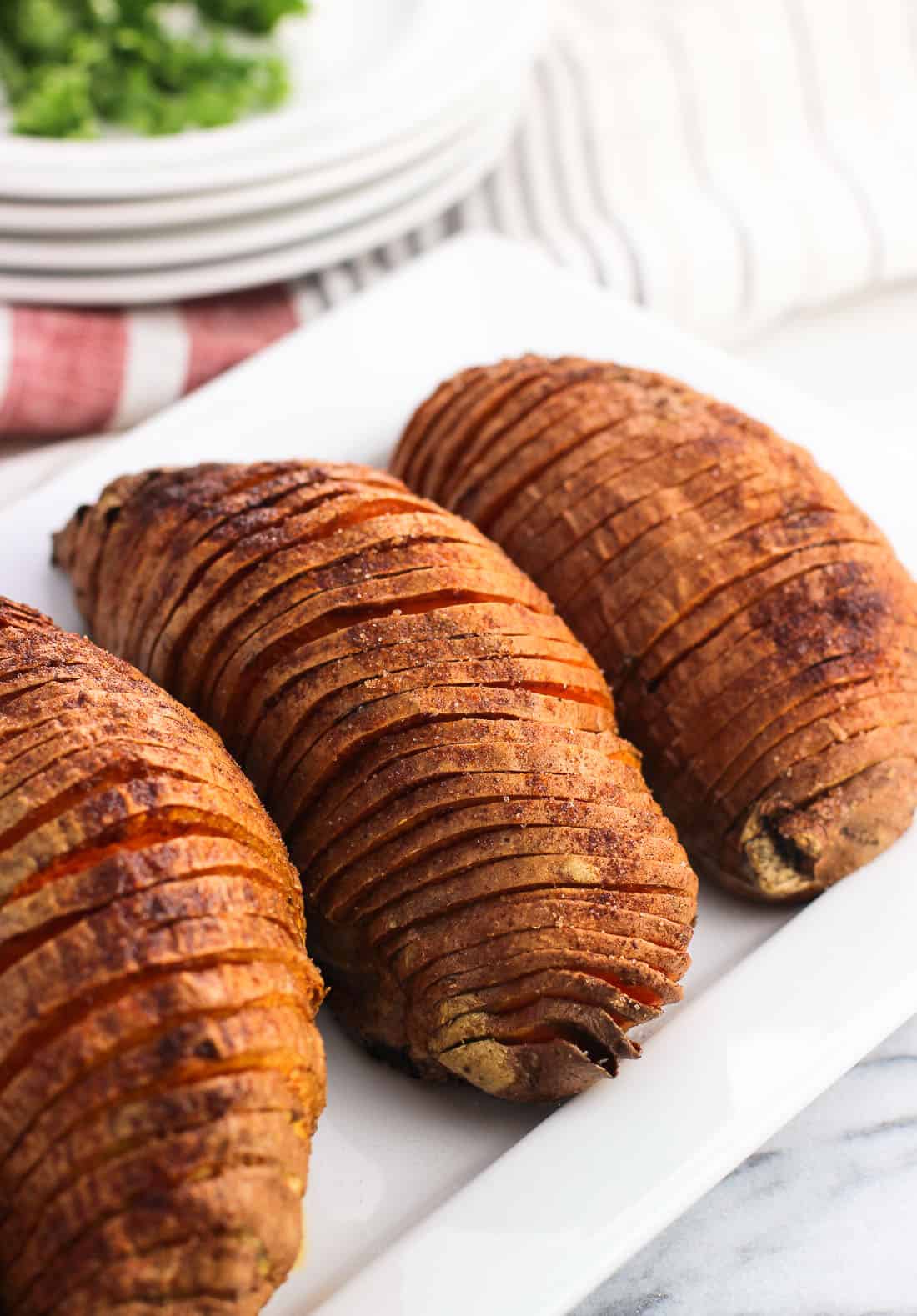 Three hasselback cut sweet potatoes on a serving dish dusted in spices