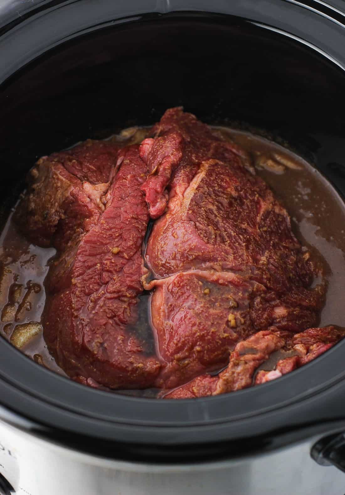 A chuck roast in the slow cooker with the rest of the ingredients before slow cooking