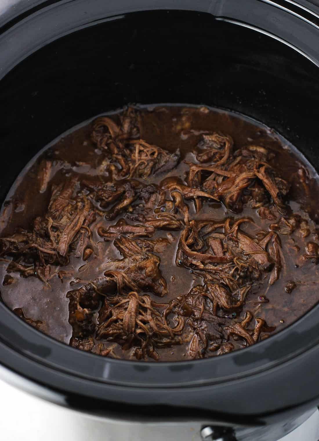 The beef shredded in sauce in the slow cooker after cooking.