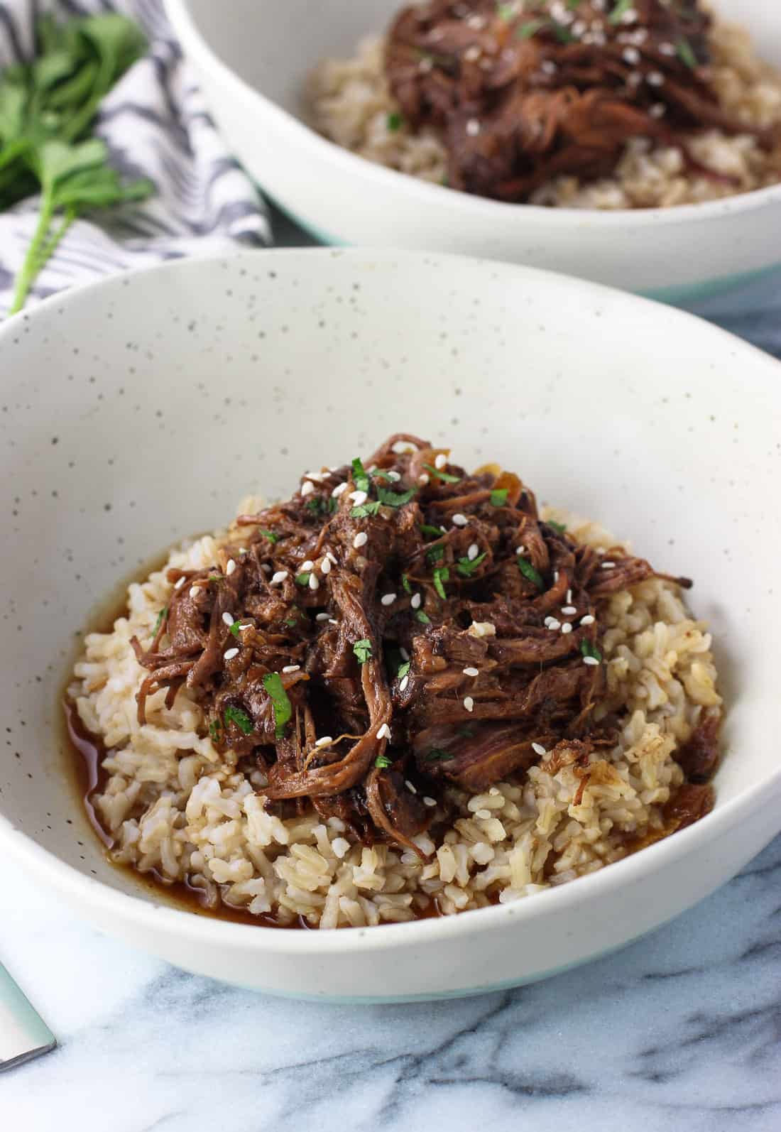 A pile of shredded beef served over brown rice in a shallow dinner bowl