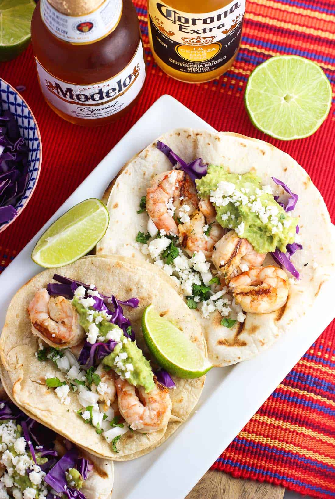 Two shrimp tacos on a tray next to limes and a bottle of beer.