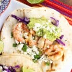 Shrimp tacos with guacamole and red onion on a tray.