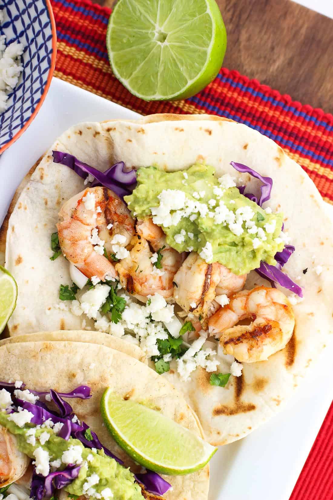 Shrimp tacos with guacamole and red onion on a tray.