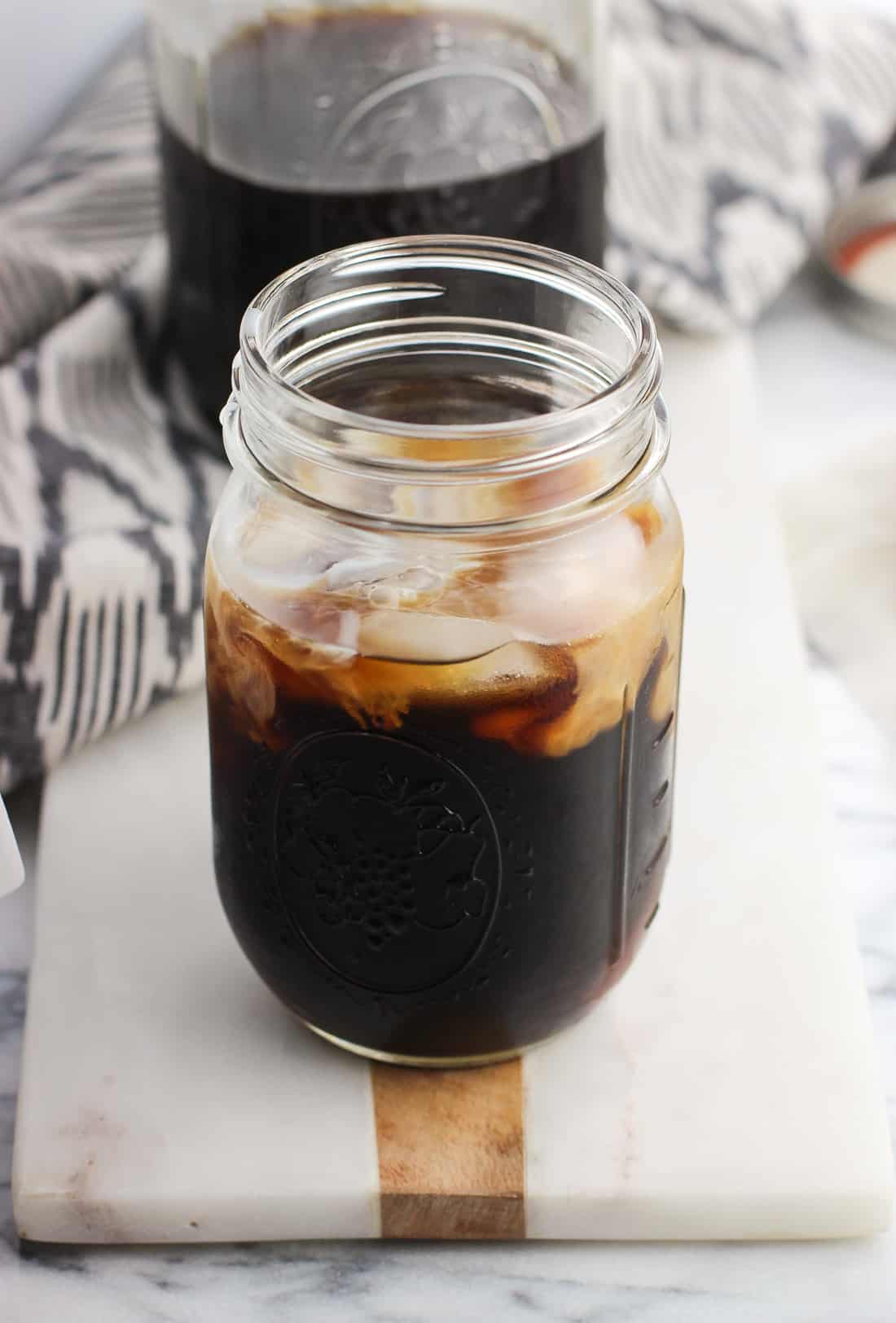 A glass mason jar filled with cold brew coffee, ice cubes, and a swirl of milk.