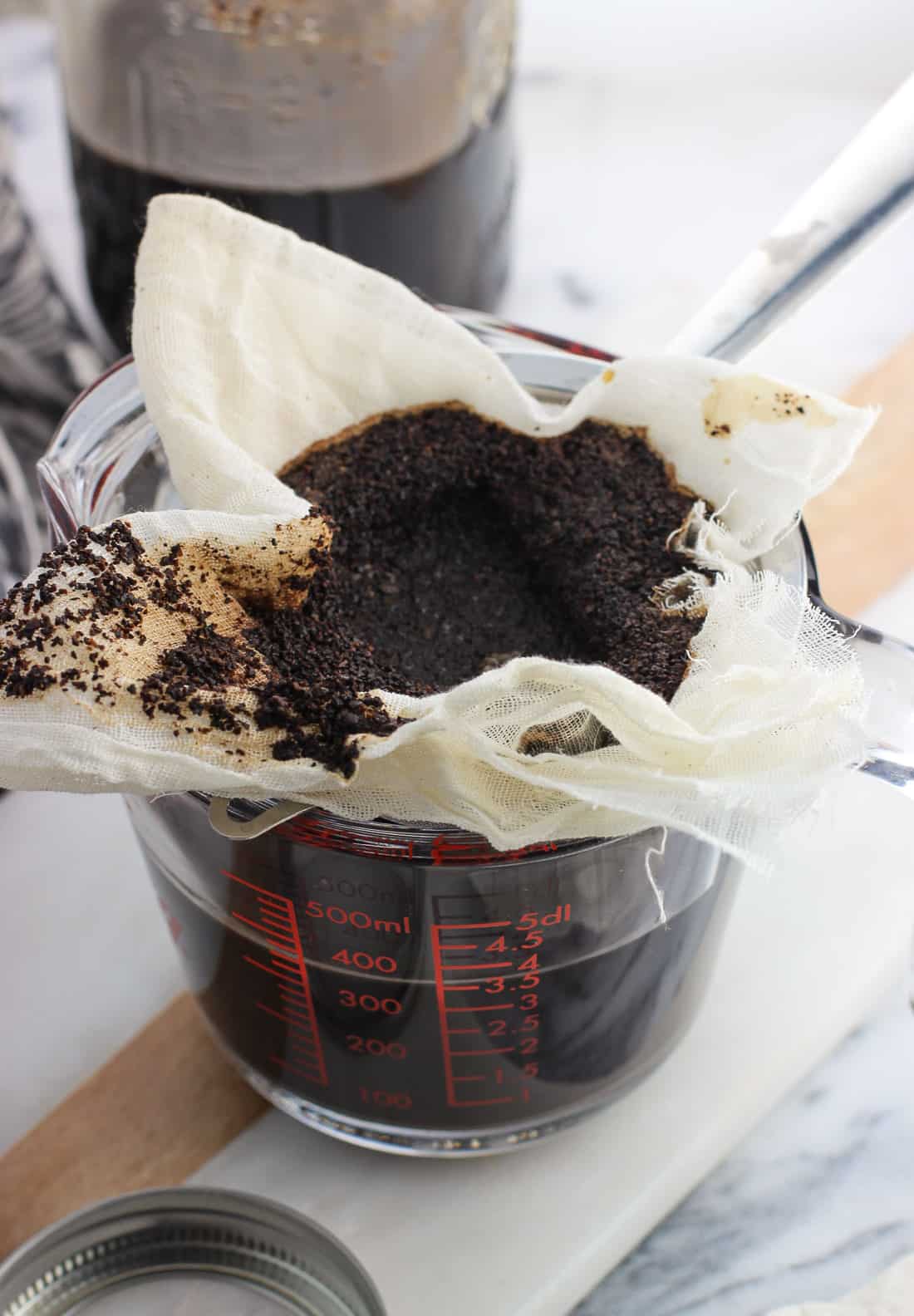 Wet coffee grounds in a cheesecloth-lined strainer set over a large glass measuring cup after the coffee has filtered through.