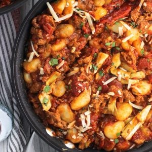 An overhead picture of a skillet full of gnocchi, crumbled Italian sausage, marinara, and artichoke hearts