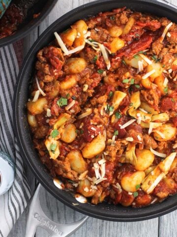 An overhead picture of a skillet full of gnocchi, crumbled Italian sausage, marinara, and artichoke hearts