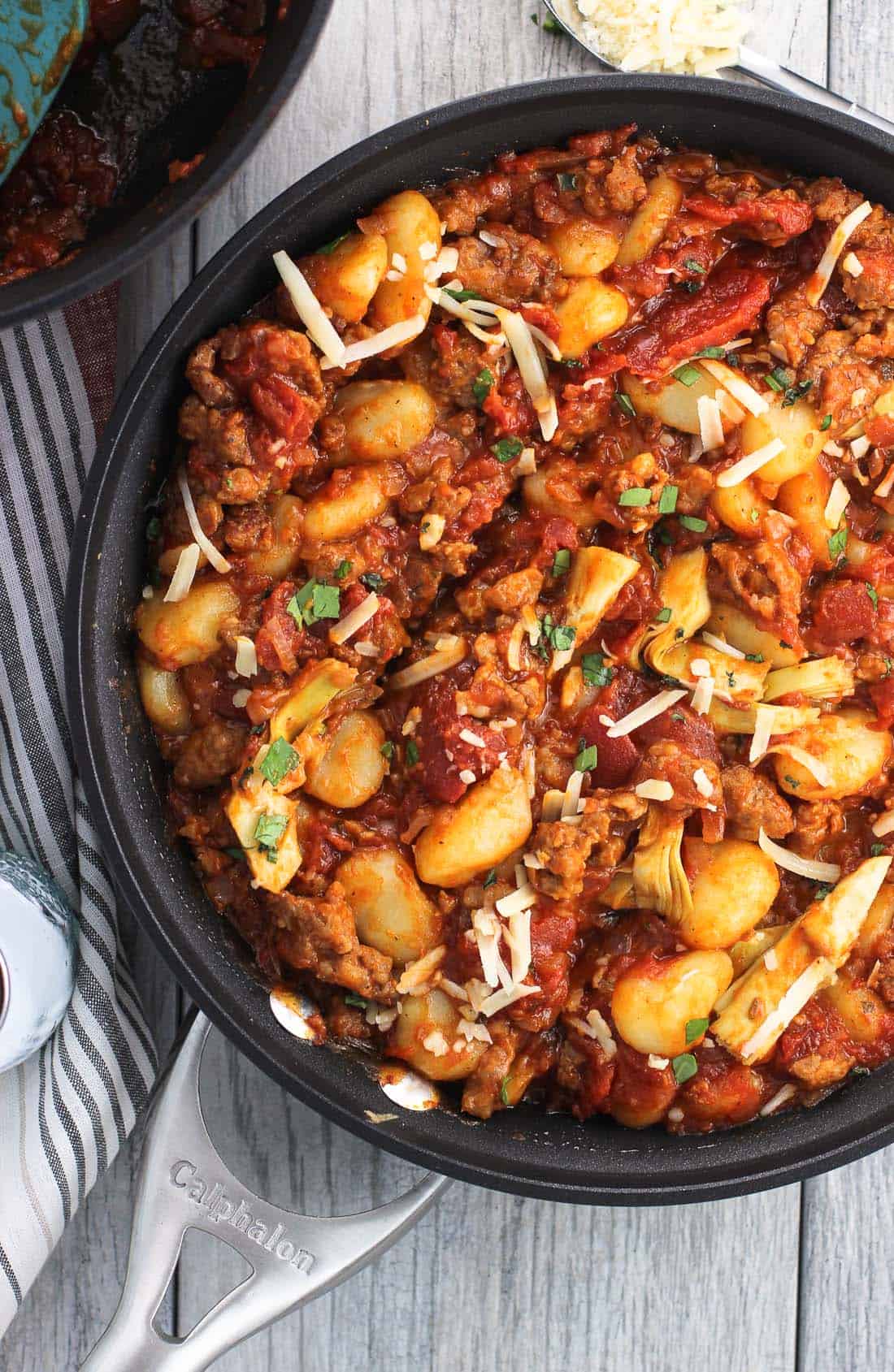 An overhead picture of a skillet full of gnocchi, crumbled Italian sausage, marinara, and artichoke hearts