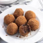 Peanut butter truffles on a small plate with a bite taken out of the front truffle.