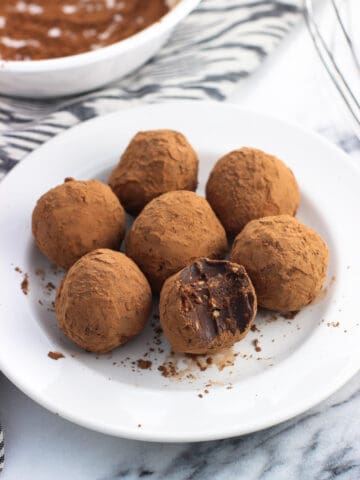 Peanut butter truffles on a small plate with a bite taken out of the front truffle.