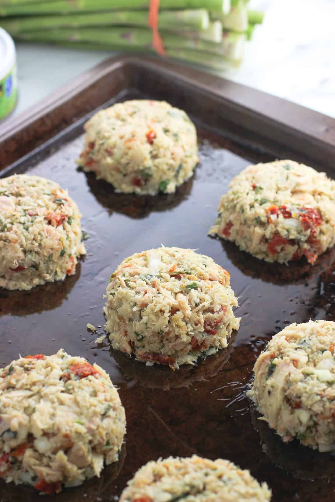 Formed tuna cake mixture on a sprayed metal baking sheet before being baked.