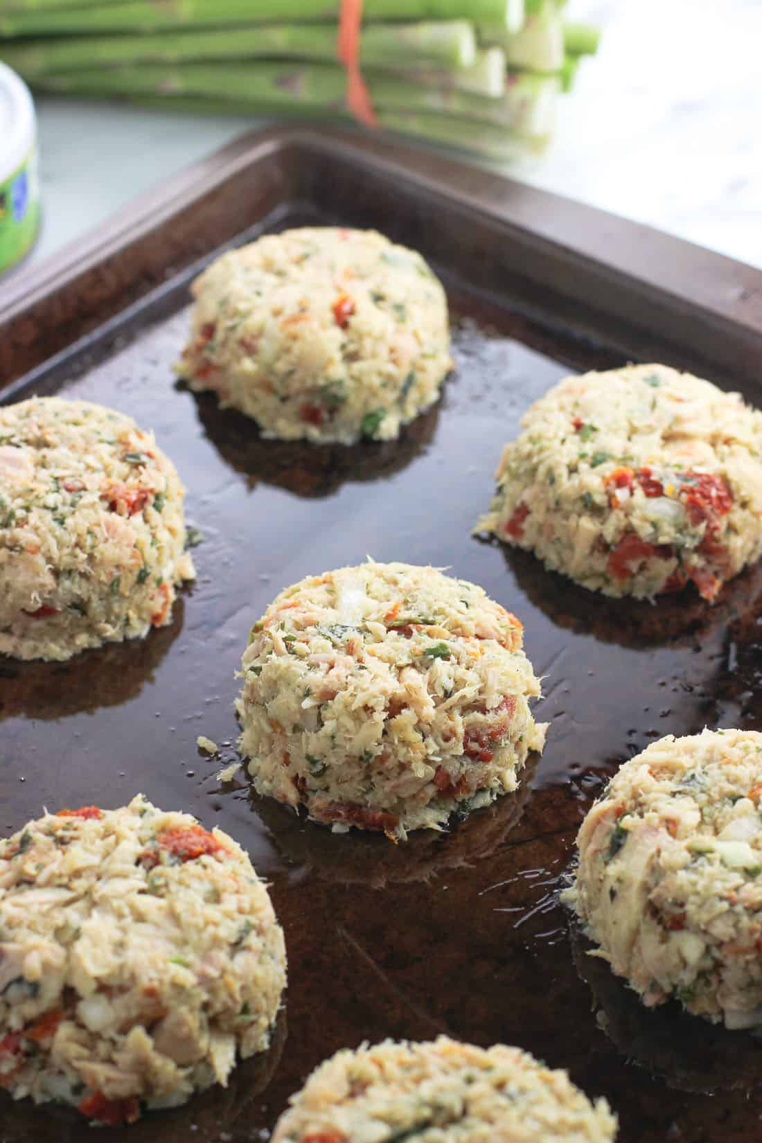 Formed tuna cake mixture on a sprayed metal baking sheet before being baked