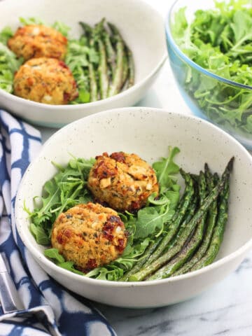 Two plates containing tuna cakes, arugula, and sauteed asparagus