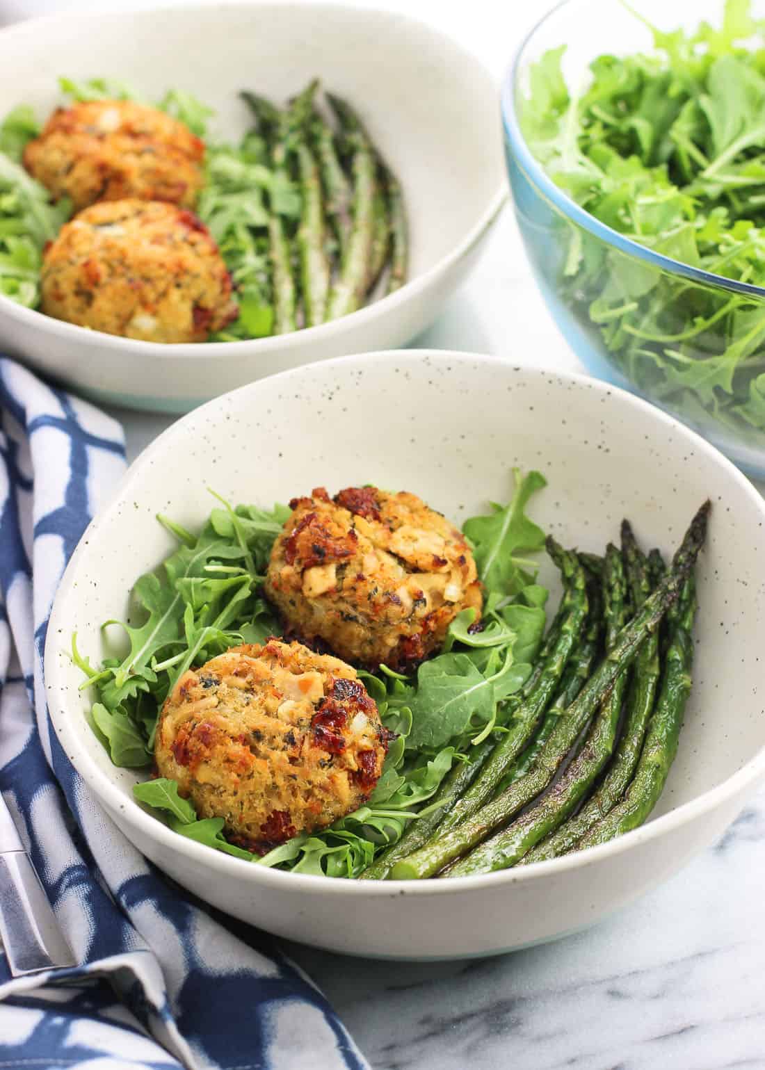 Two plates containing tuna cakes, arugula, and sauteed asparagus