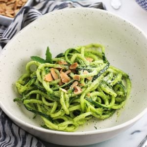 Zucchini noodles in a bowl covered in mint pesto sauce and garnished with toasted slivered almonds