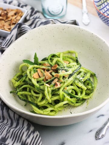 Zucchini noodles in a bowl covered in mint pesto sauce and garnished with toasted slivered almonds