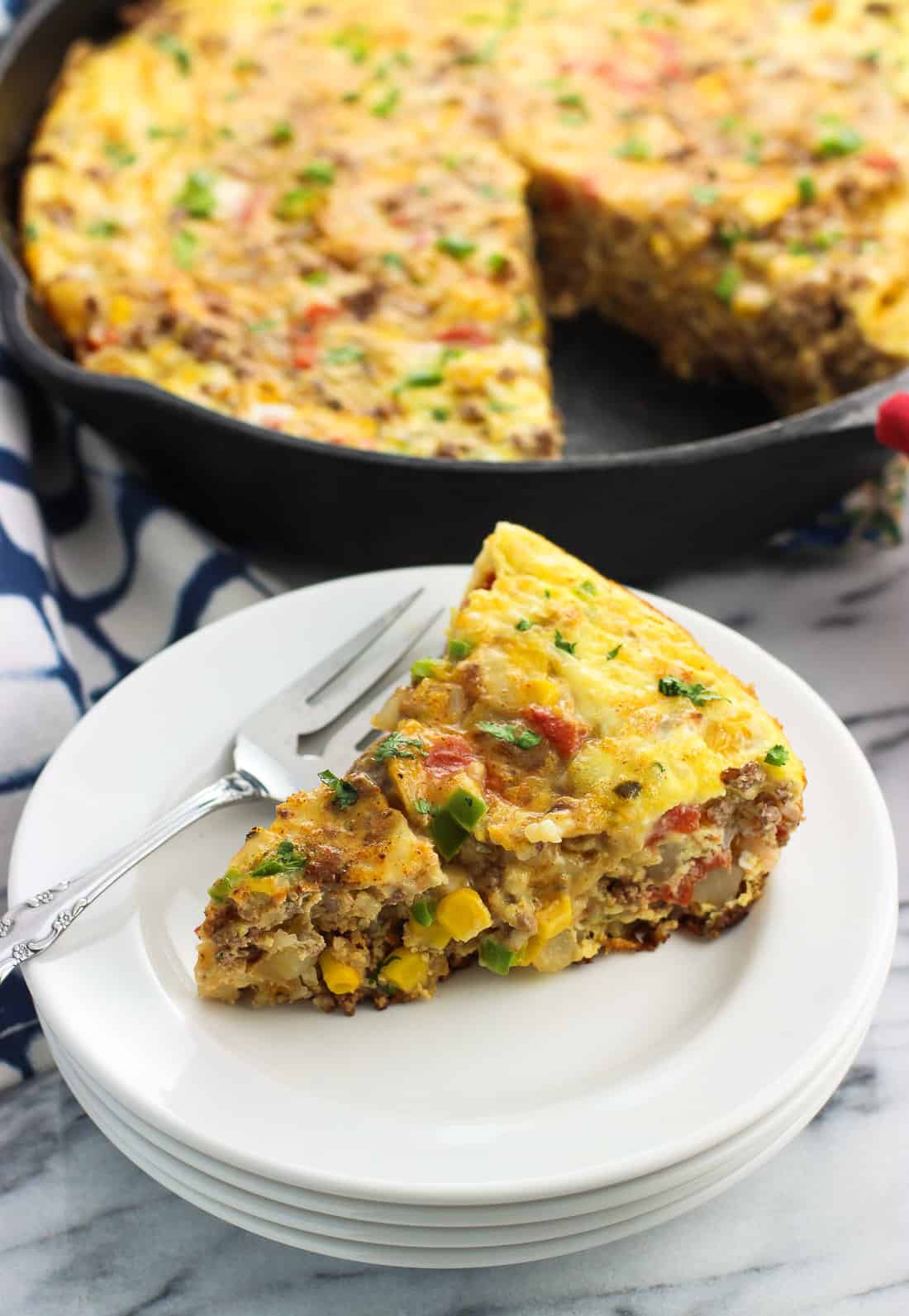 A slice of frittata on a plate in front of the pan.