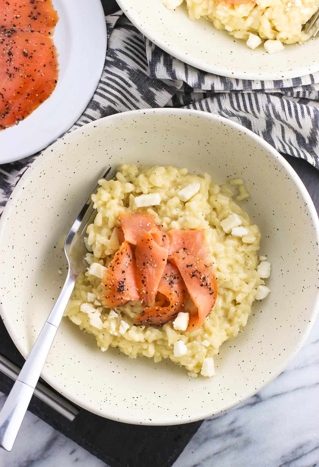 Feta risotto in a shallow bowl topped with smoked salmon slices.