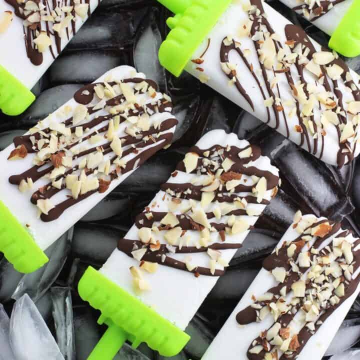 Six coconut popsicles drizzled with chocolate set on an ice cube lined baking sheet