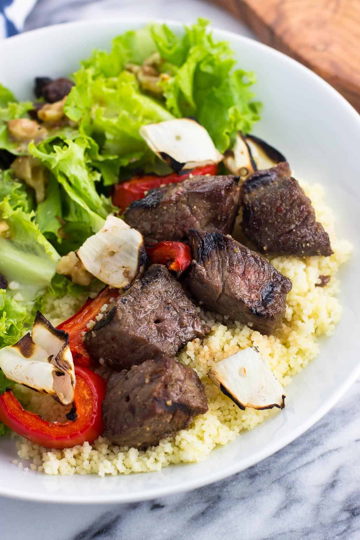Grilled steak cubes served over couscous with grilled vegetables and a side salad.