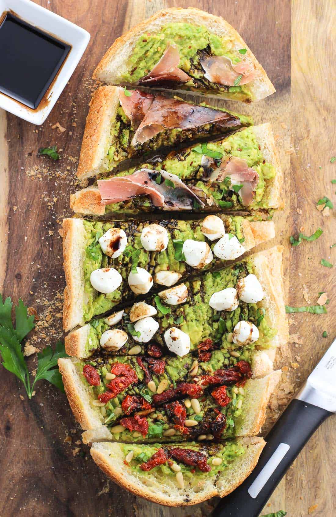 An overhead shot of a half-loaf of avocado garlic toast cut into wedges next to a small dish of balsamic glaze