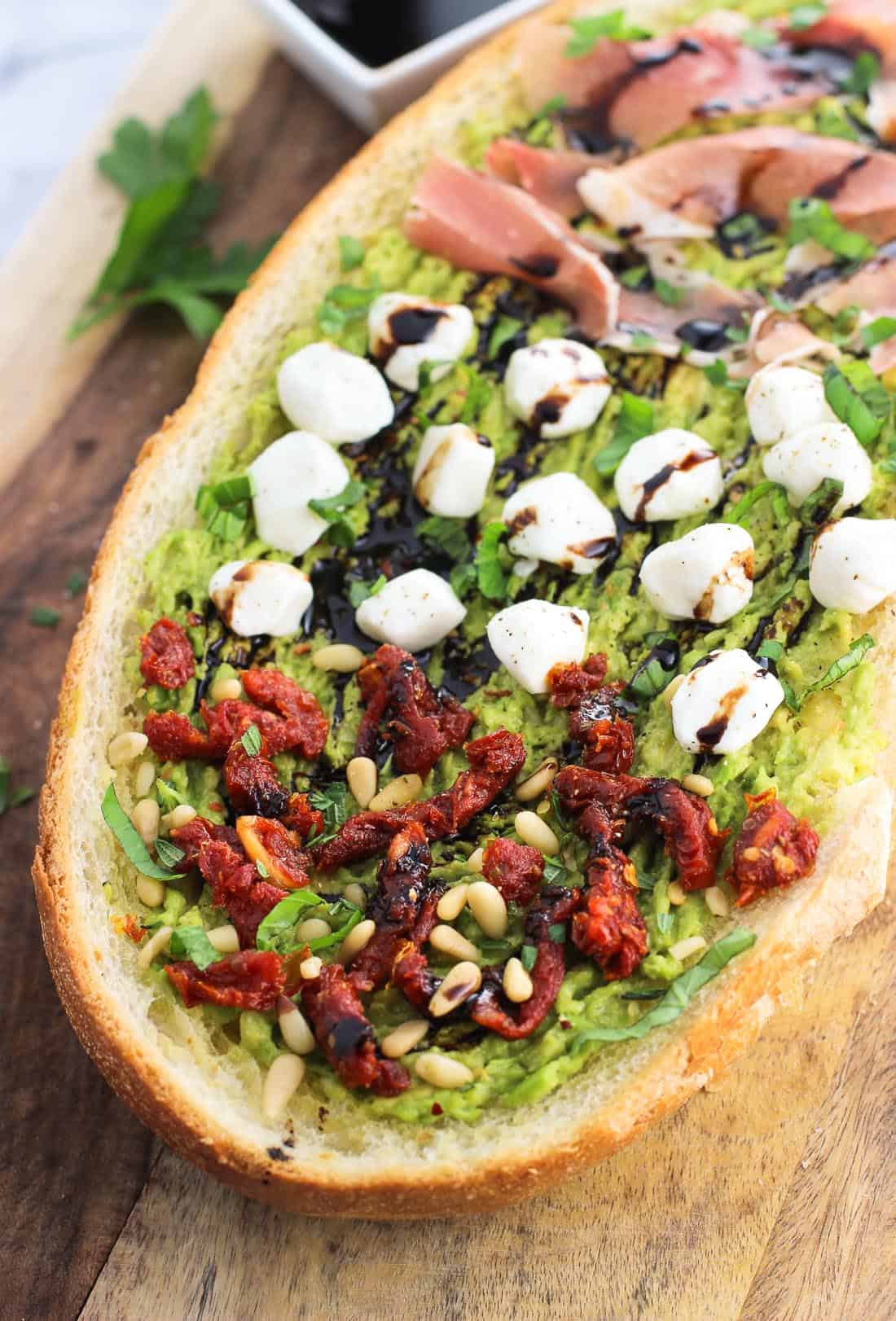 A slab of avocado garlic bread with various toppings.