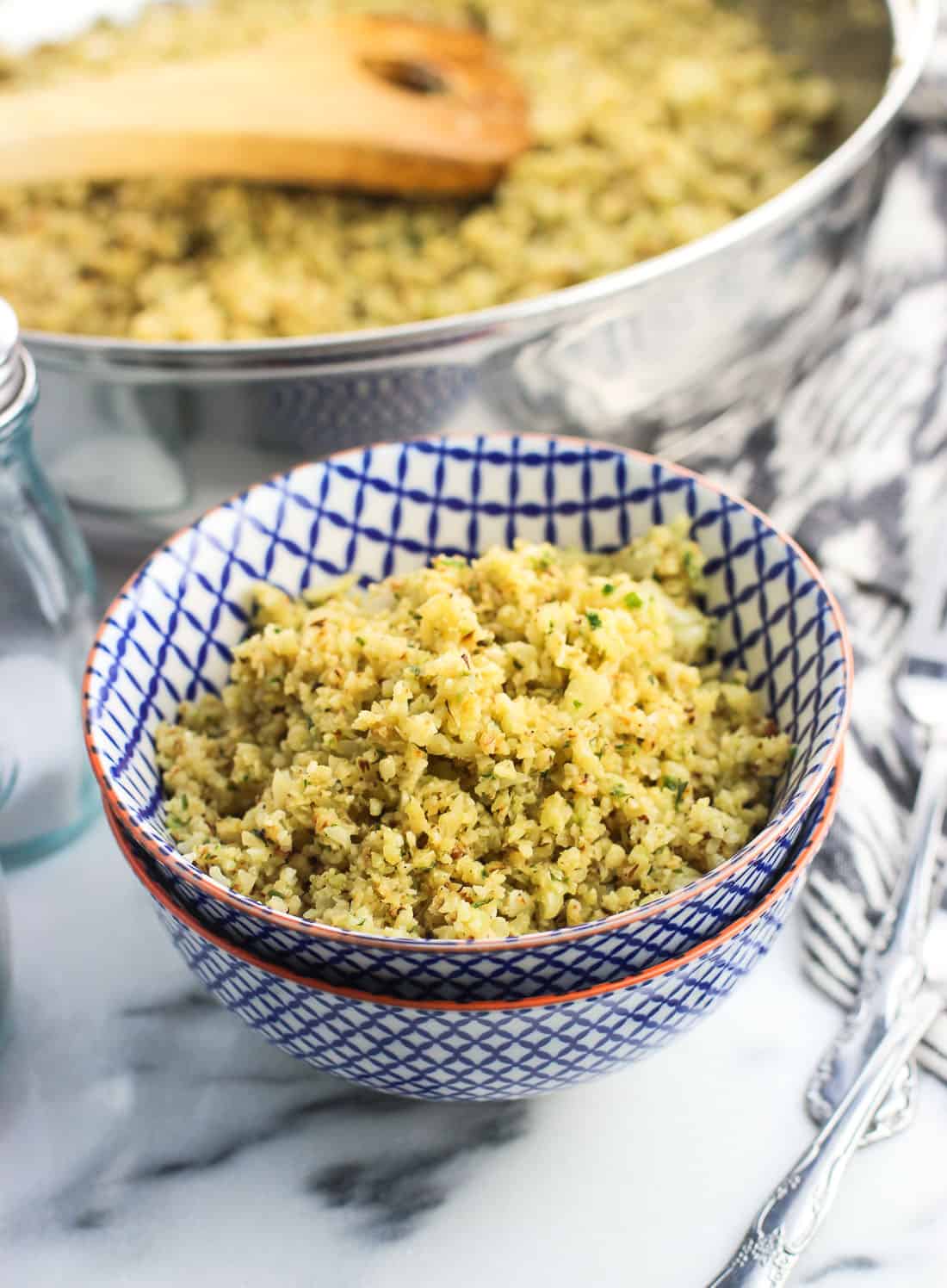 Cauliflower rice in a small bowl next to the pan and salt and pepper shakers.