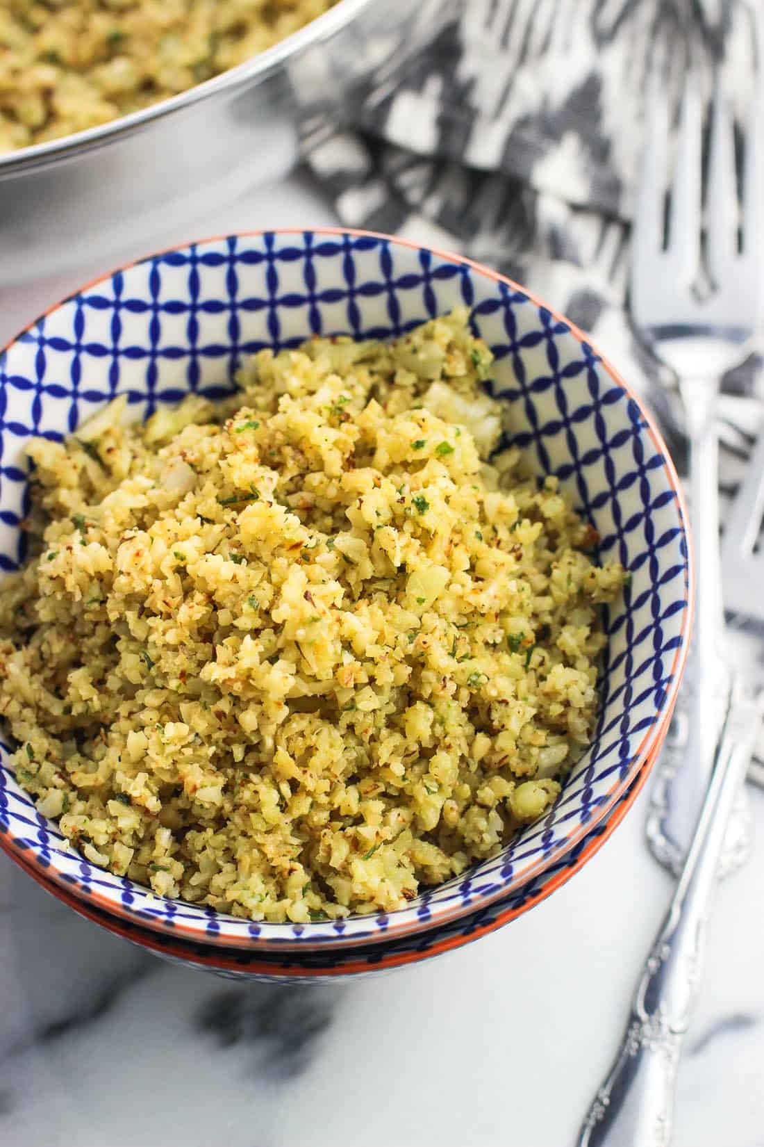 A close-up of a serving of pesto cauliflower rice in a bowl next to forks.