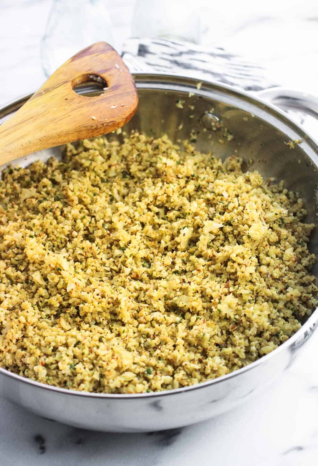 A pan of seasoned cauliflower rice in a bowl with a wooden spoon.