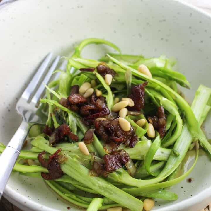 Shaved asparagus in a bowl topped with bacon vinaigrette and pine nuts.
