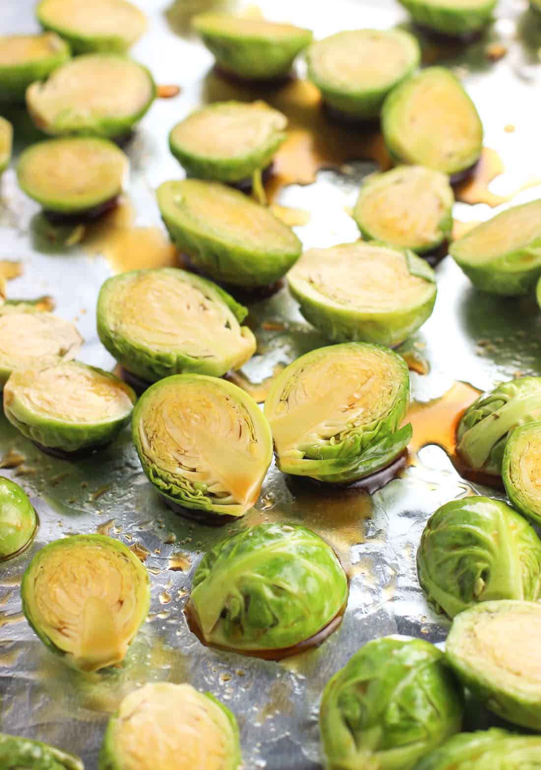 Halved Brussels sprouts on a foil-lined baking sheet tossed in glaze before roasting