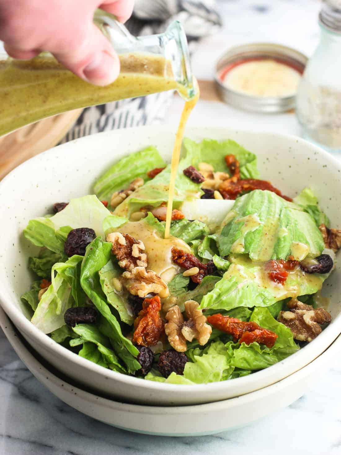 A jar of honey mustard vinaigrette being poured over a salad