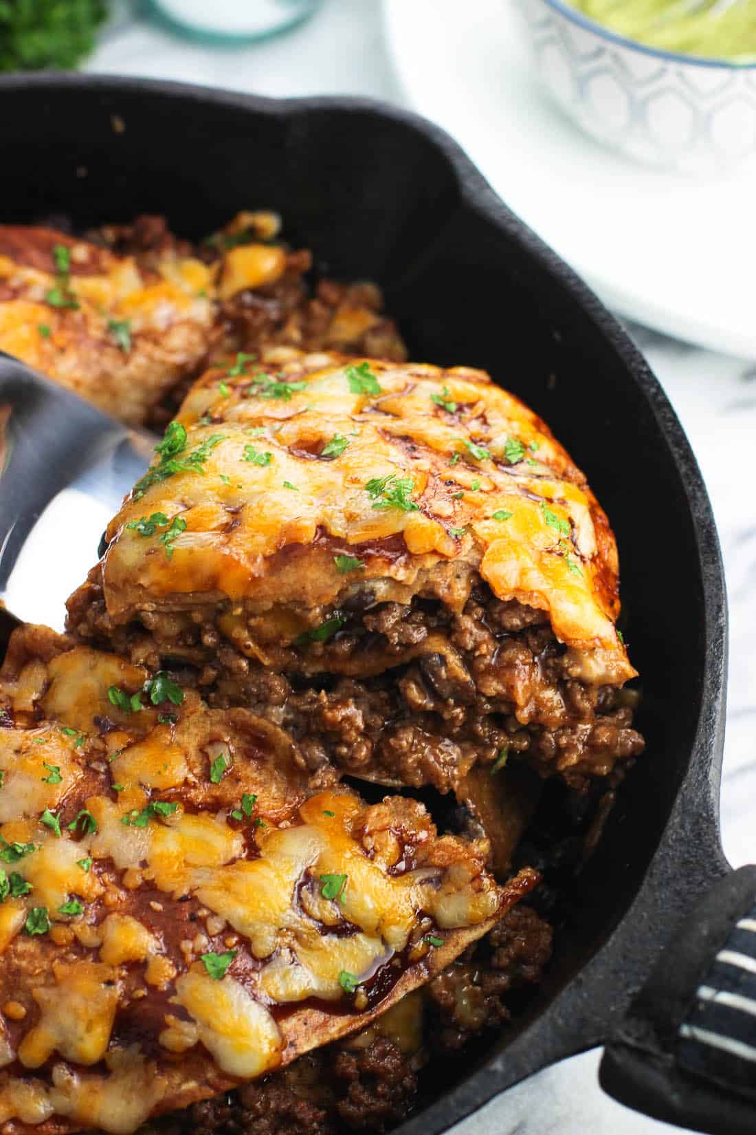 A wedge of beef tortilla pie being lifted by a spatula out of a cast iron pan to show the different layers.