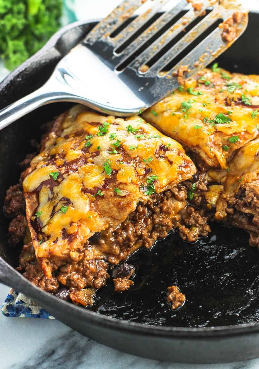 Beef tortilla pie in a cast iron skillet with one wedge removed, with a metal spatula resting on top.