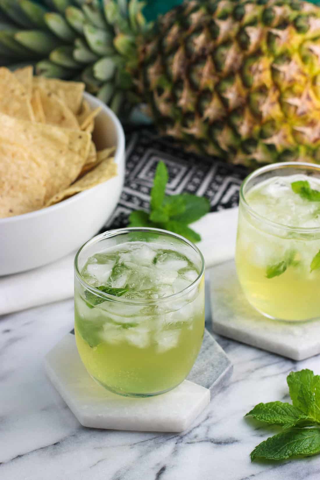 Vodka sodas on marble coasters next to fresh fruit and a bowl of tortilla chips.