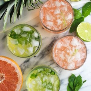 Four vodka sodas (two grapefruit, two pineapple) in small glasses surrounded by fruit.