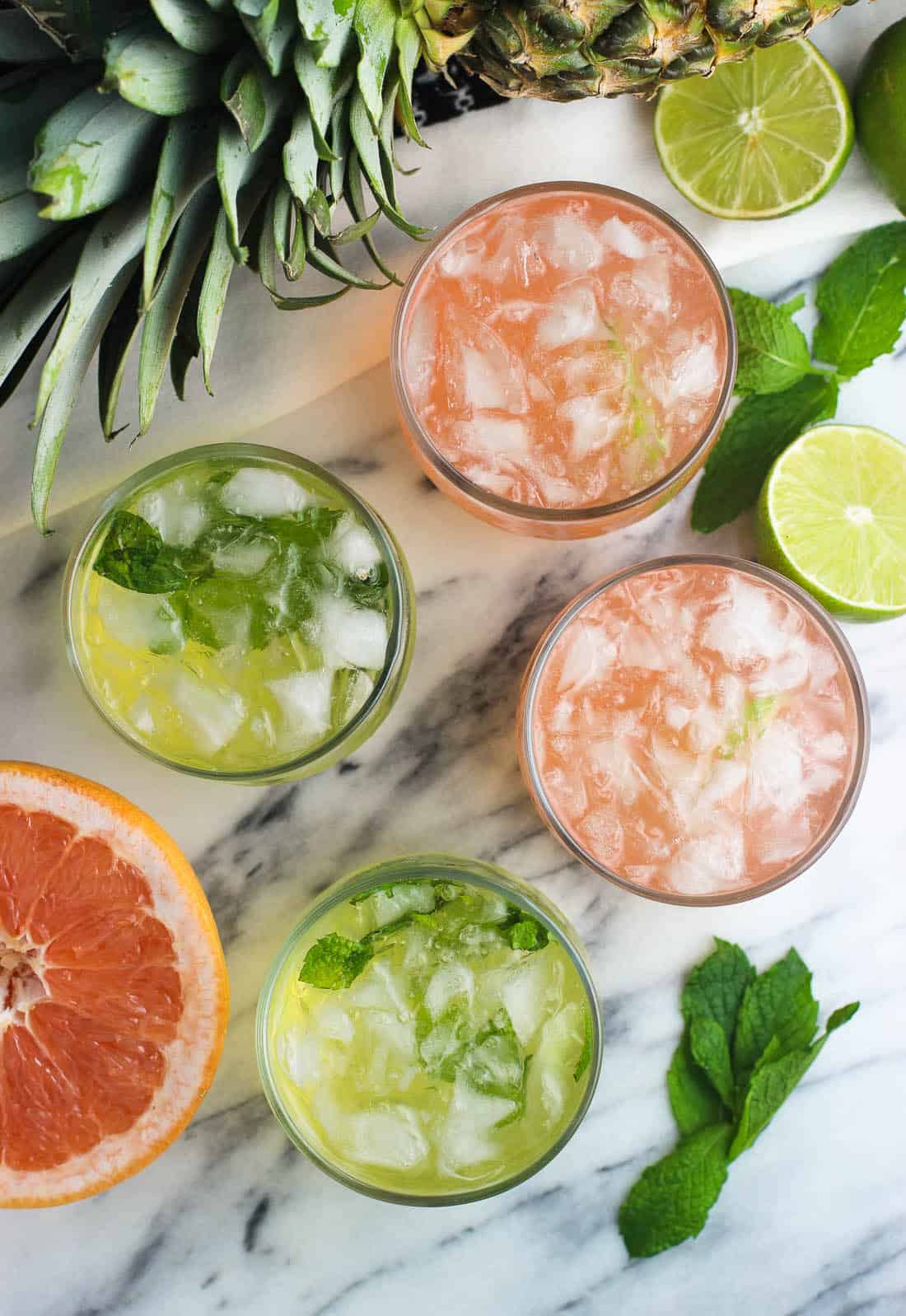 Four vodka sodas (two grapefruit, two pineapple) in small glasses surrounded by fruit.