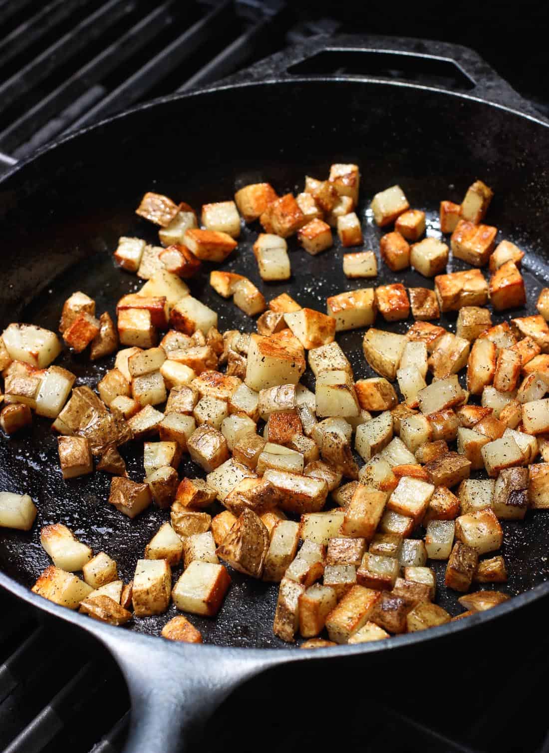 A cast iron pan filled with roasted potato cubes on a grill.