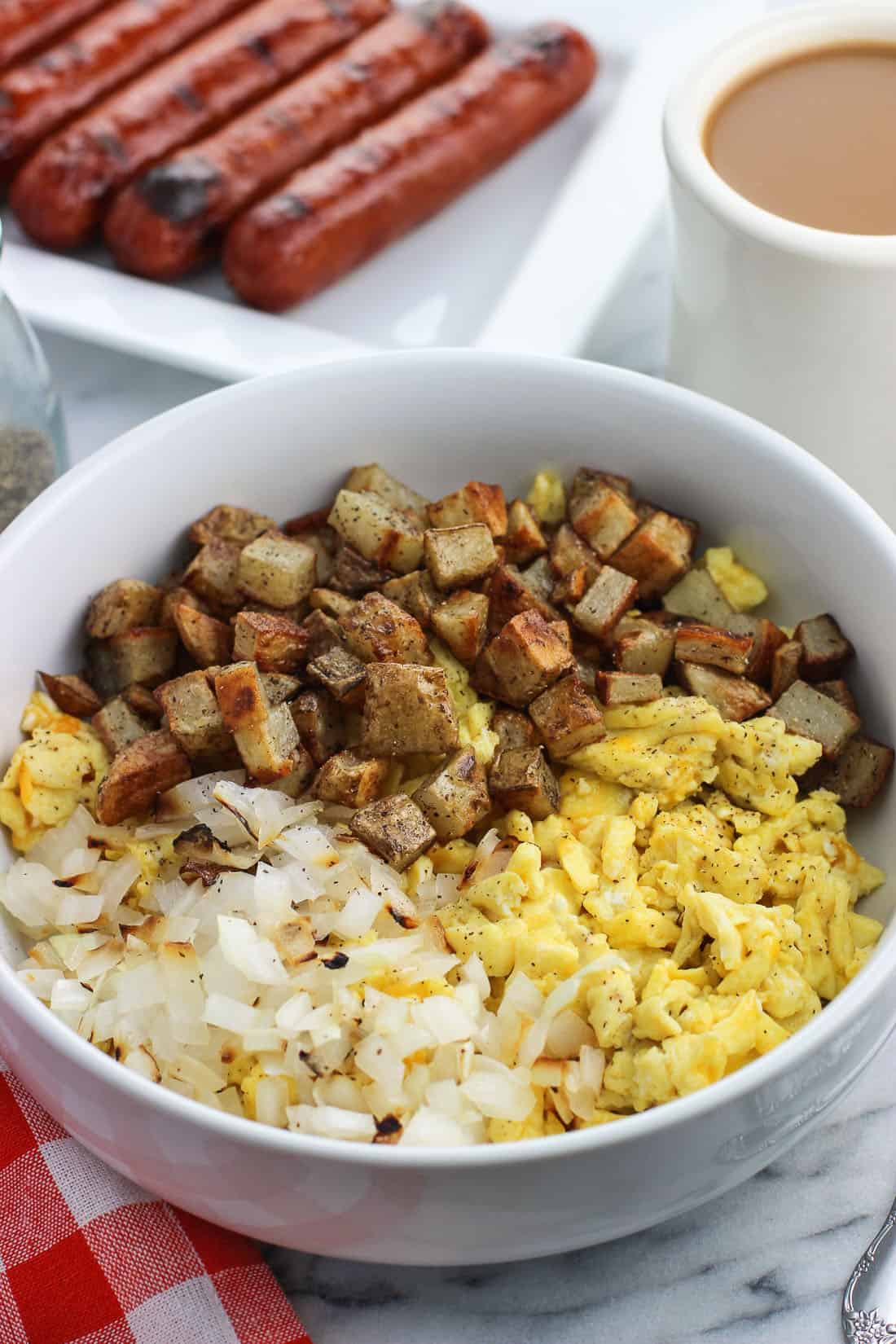 A big bowl featuring sections of grilled onion, scrambled eggs, and roasted potatoes.