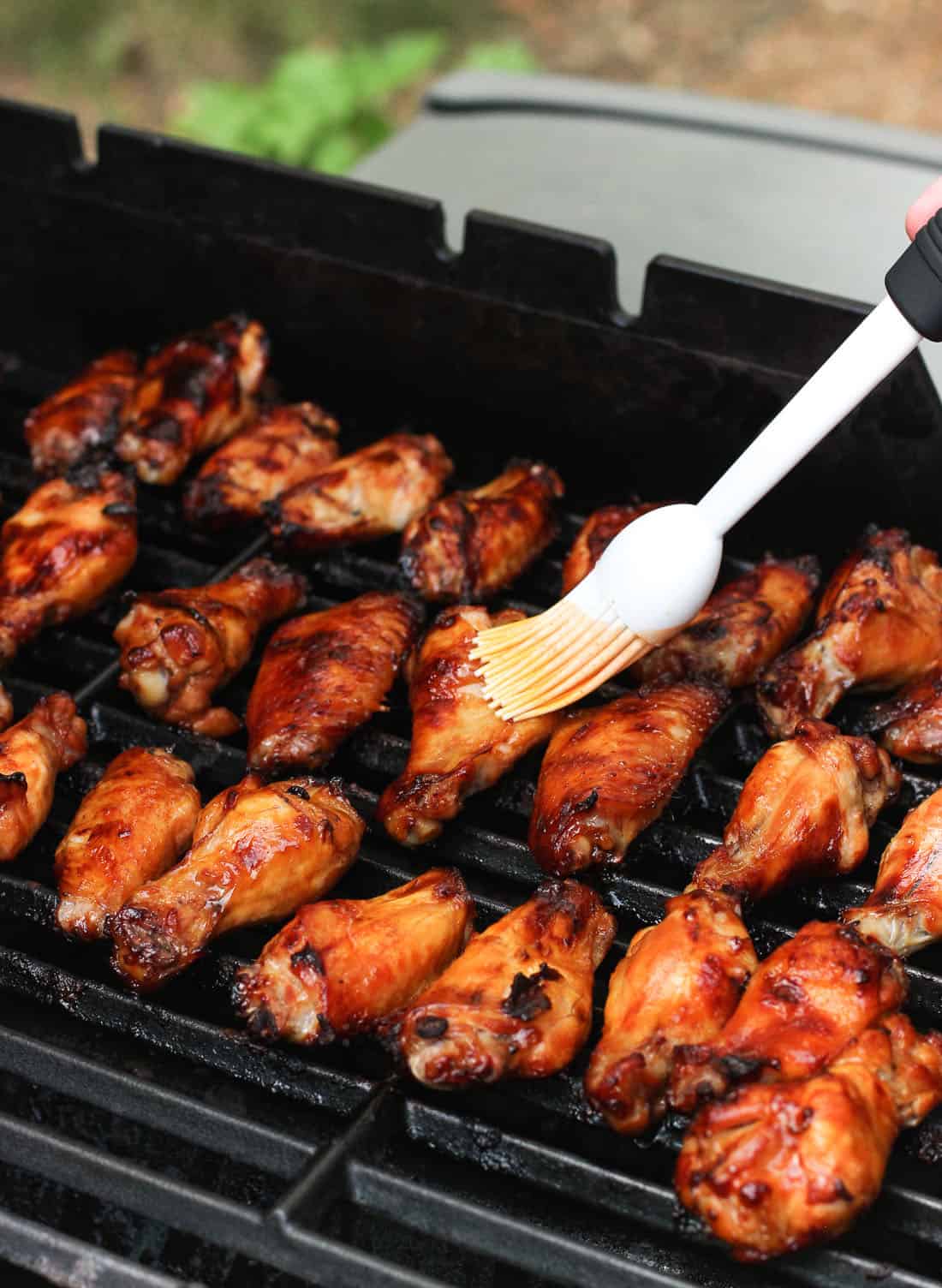 A hand brushing hot sauce on the cooked wings on a grill.