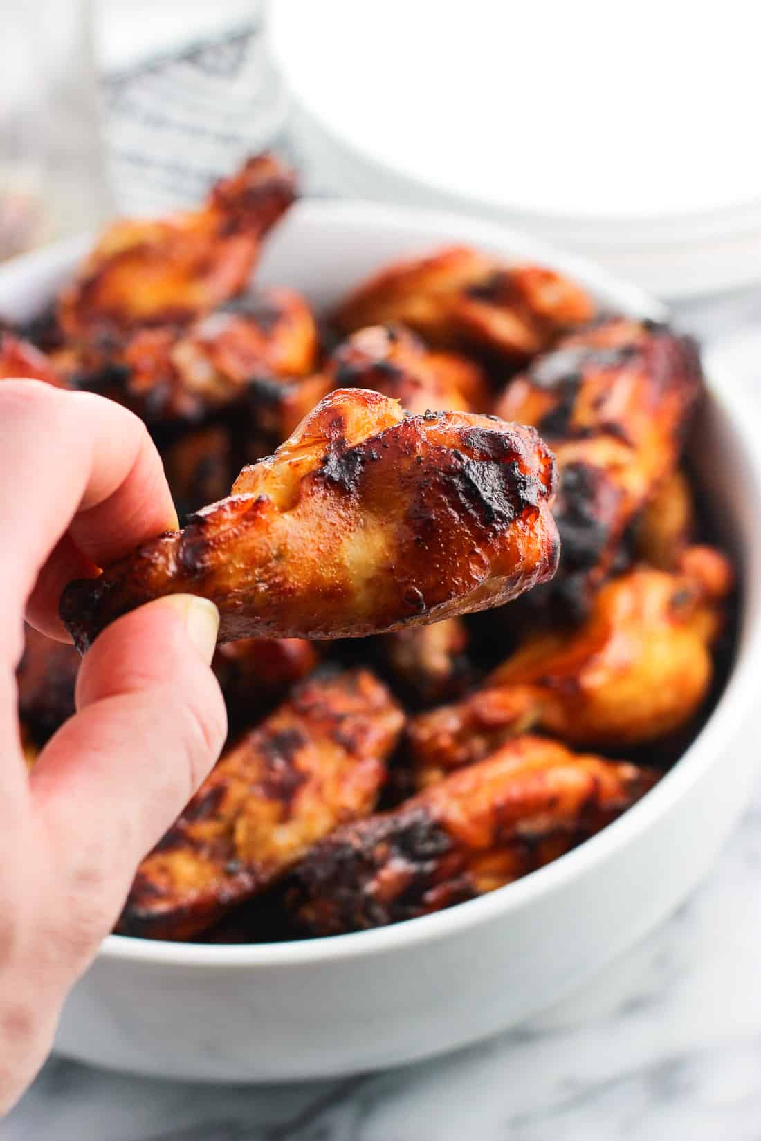 A hand lifting a grilled drumette wing out of the serving bowl.