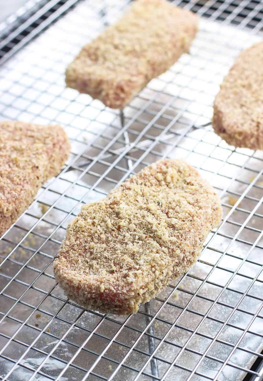 Crusted pork chops on a wire rack set over a baking sheet before going in the oven