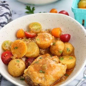 A chicken thigh, roasted potatoes, tomatoes, and sauce in a dinner bowl.