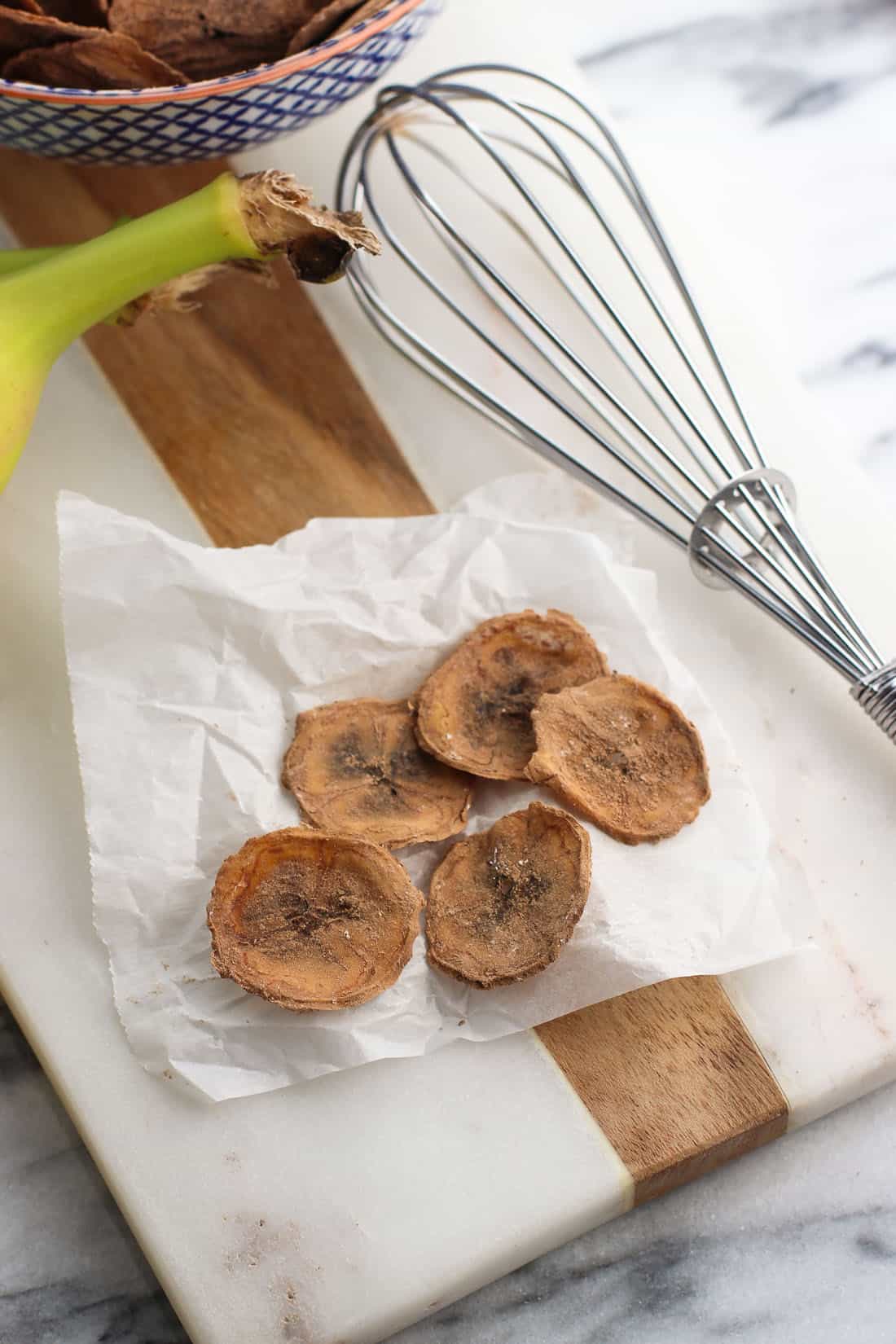 Five banana chips on a small piece of crumbled parchment paper on a marble board